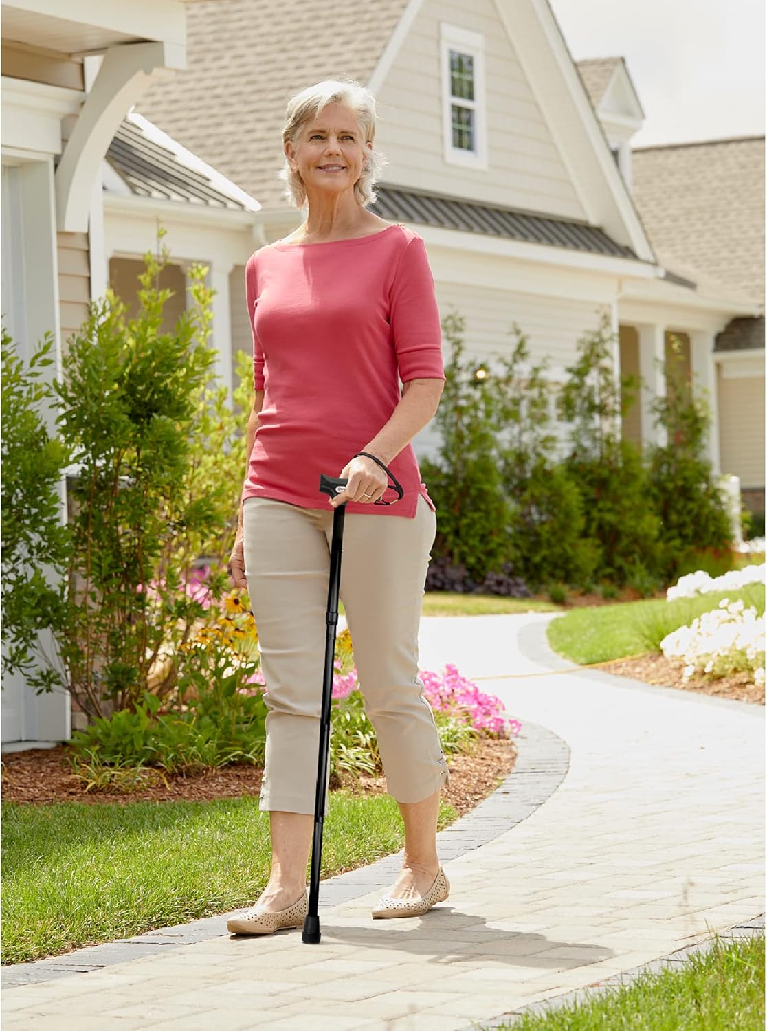 Woman walking with a cane on a sidewalk in front of a house